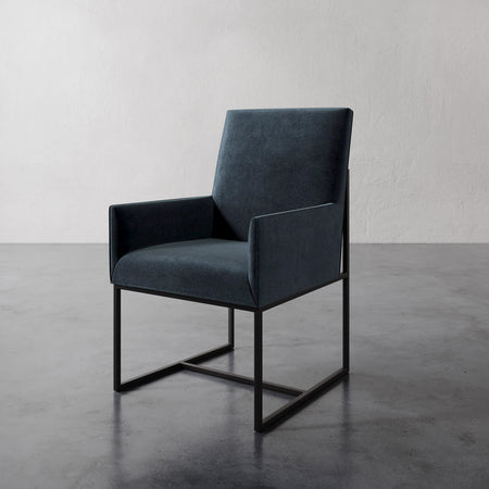 Lemieux et Cie Dupont Dining Arm Chair in charcoal upholstery with dark geometric sled base, shown on polished concrete floor against neutral plaster walls.