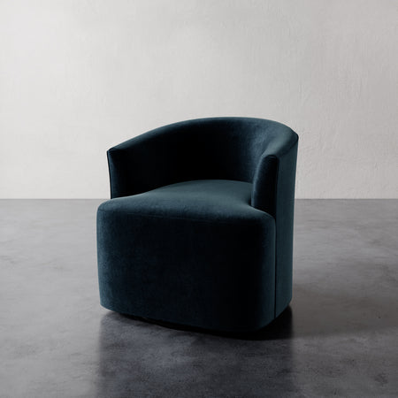 Lemieux et Cie Garnier Swivel Chair in deep teal upholstery, rounded sculptural form on polished concrete floor against neutral plaster wall.