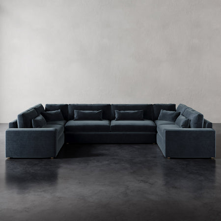 Lemieux et Cie Lacroix U-Sectional in charcoal upholstery, modular sofa with deep cushions and bolster pillows, shown on dark concrete floor against white walls.