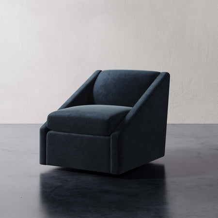 Lemieux et Cie Fontaine Swivel Chair in deep teal upholstery, sculptural swivel chair with angled arms, shown on dark wood floor against white plaster walls.