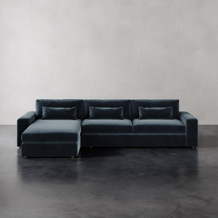 Lemieux et Cie Lacroix Left Chaise Sectional in dark teal velvet, low-profile modular sofa with bolster pillows on dark concrete floor.