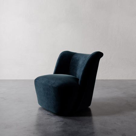 Lemieux et Cie Aurélie Swivel Chair in deep teal, sculptural rounded form with rolled back, shown on polished concrete floor against textured plaster wall.