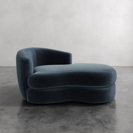 Lemieux et Cie Rulmann Left Arm Chaise in deep blue upholstery, sculptural low-slung chaise with curved organic form, on polished concrete floor against neutral plaster wall.
