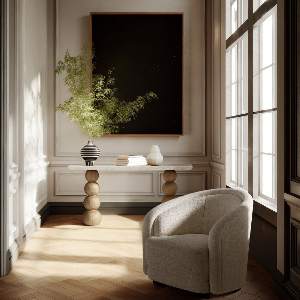 Lemieux et Cie Chloé Console Table, stacked sphere-base design with stone top, styled with books and vase in paneled room with herringbone floors and bright sunlight.