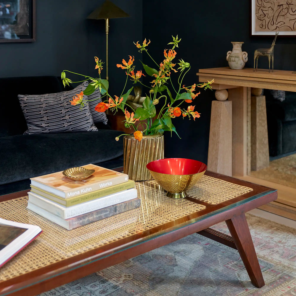 Living room with a vintage Pierre Jeanneret daybed coffee table, books, a vase with flowers, and a dark wall.