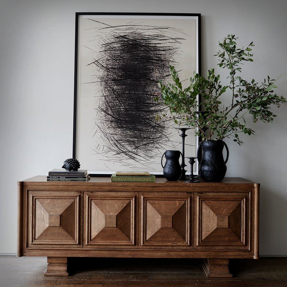 Lemieux et Cie Voltaire Sideboard with geometric paneled doors, styled with abstract art and dark vases on warm-toned wood floors against neutral walls.