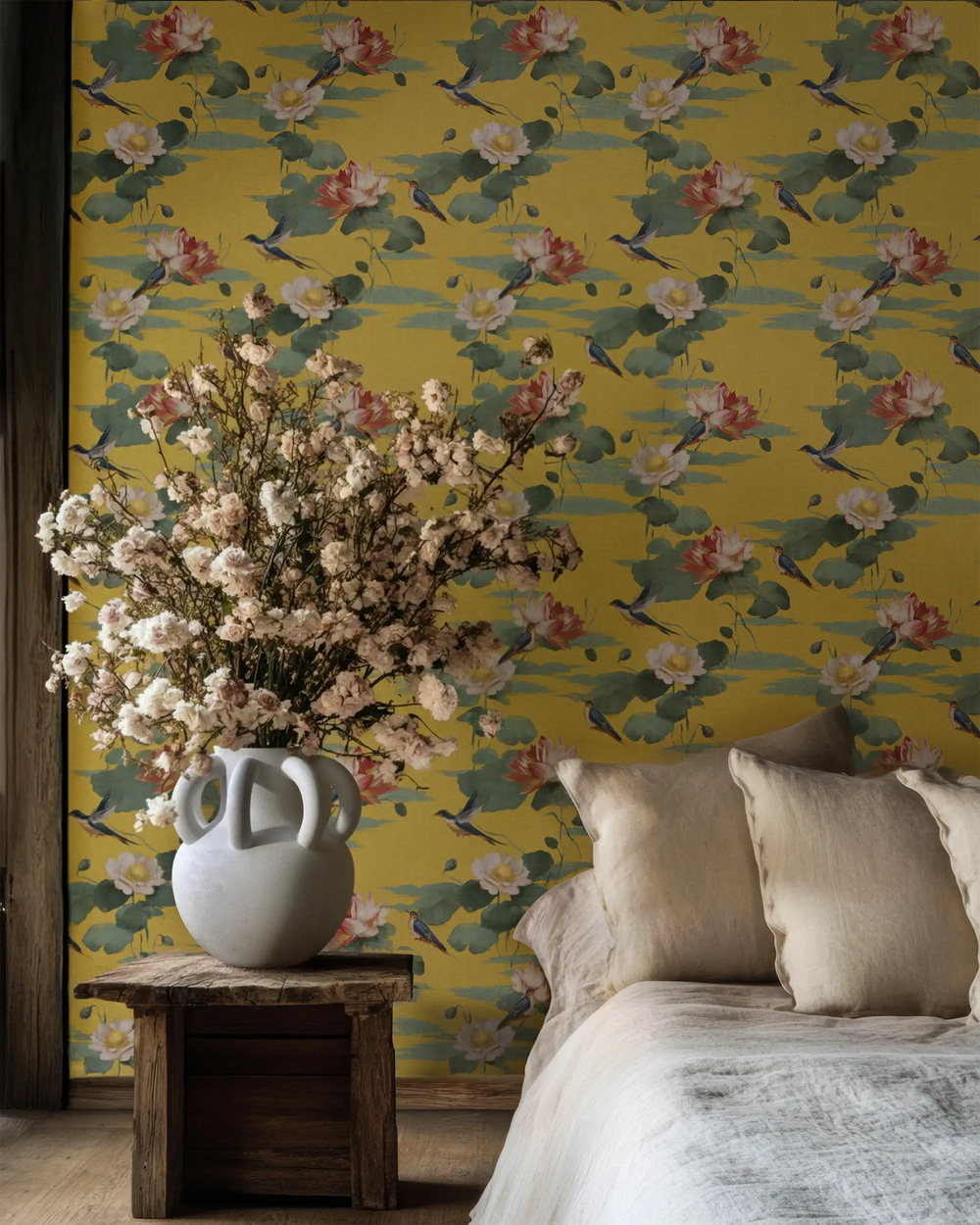 Bedroom styled with Lemieux et Cie Lily Pond chinoiserie peel and stick wallpaper, featuring gold floral detailing, a wooden side table with fresh flowers, and beige accent pillows, an elegant Asian inspired luxury wallpaper design.
