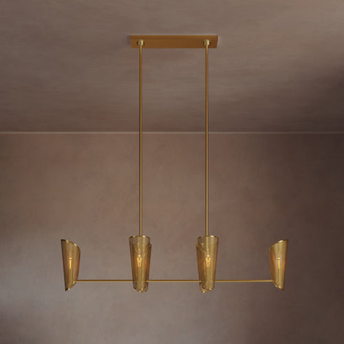 Lemieux et Cie chandelier with four tapered shades suspended from warm brass rods, shown against neutral plaster walls in soft ambient light.