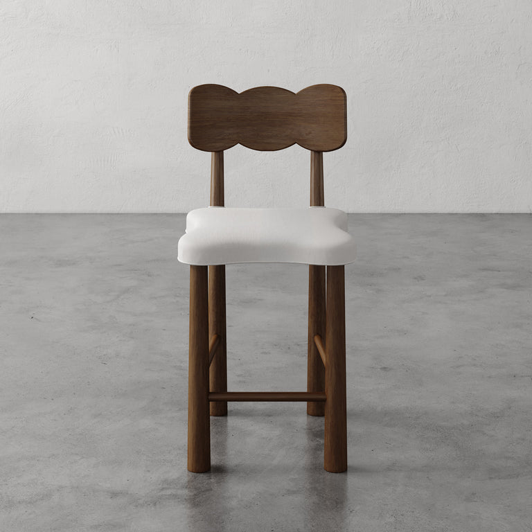 Lemieux et Cie Madeleine Counter Stool with sculpted backrest and upholstered seat, counter-height chair shown on concrete floor against textured plaster walls.