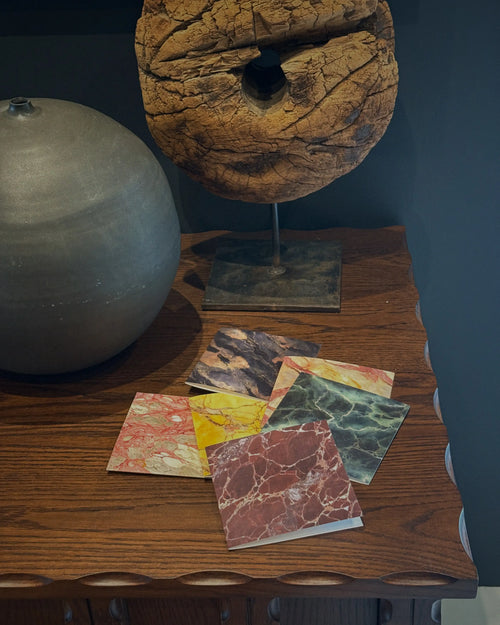 Lemieux et Cie Rosa Portogallo Greeting Card Set, marbled paper cards in coral, yellow, green and blue, styled on wood table with ceramic vase and sculptural aged wood object against dark wall.