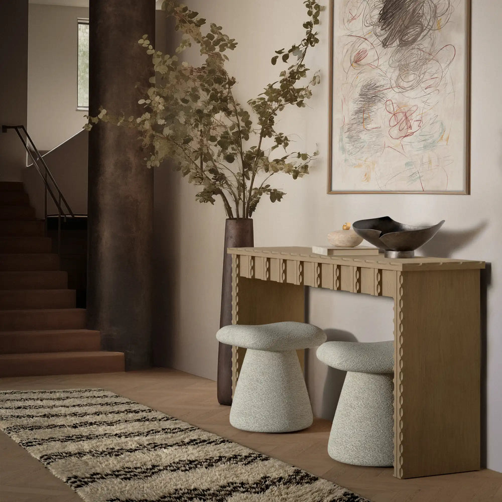 Lemieux et Cie Marchand Console Table in walnut with scalloped edges, styled with sculptural stools and black bowl in neutral entry with wood floors and artwork.