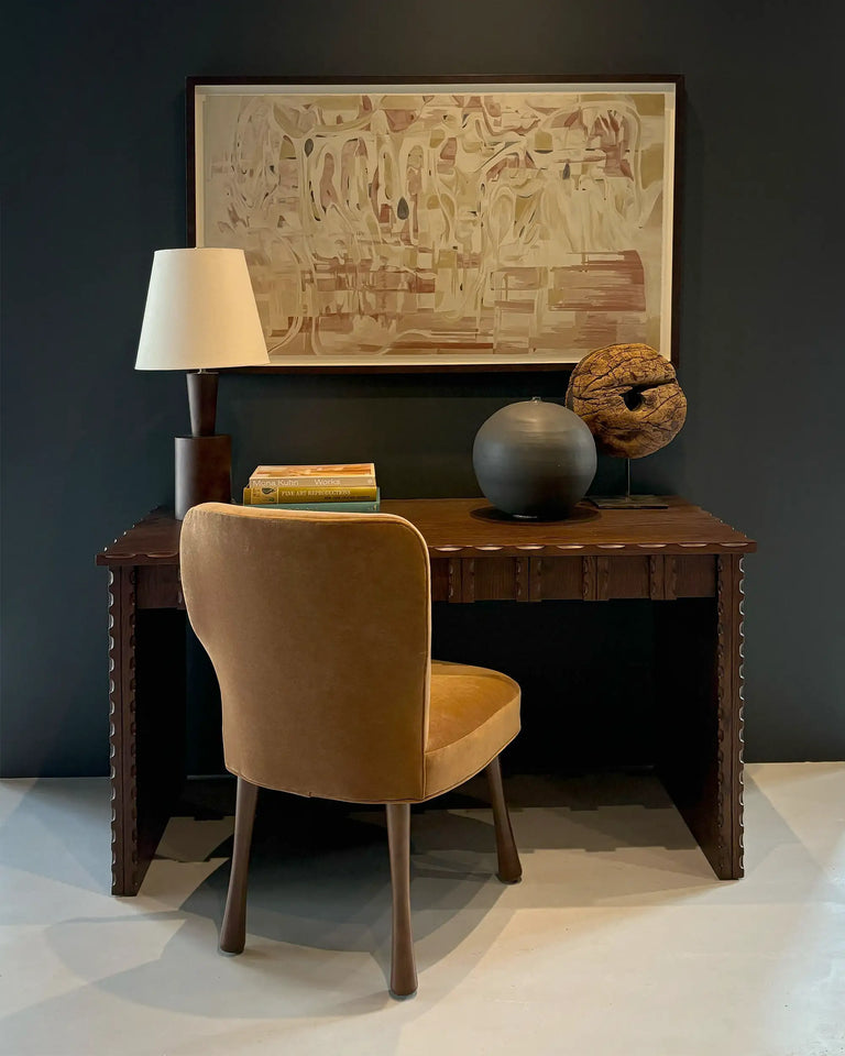 Lemieux et Cie Marchand Desk in walnut oak finish, carved desk styled with warm upholstered chair, table lamp, and abstract art against dark teal walls.