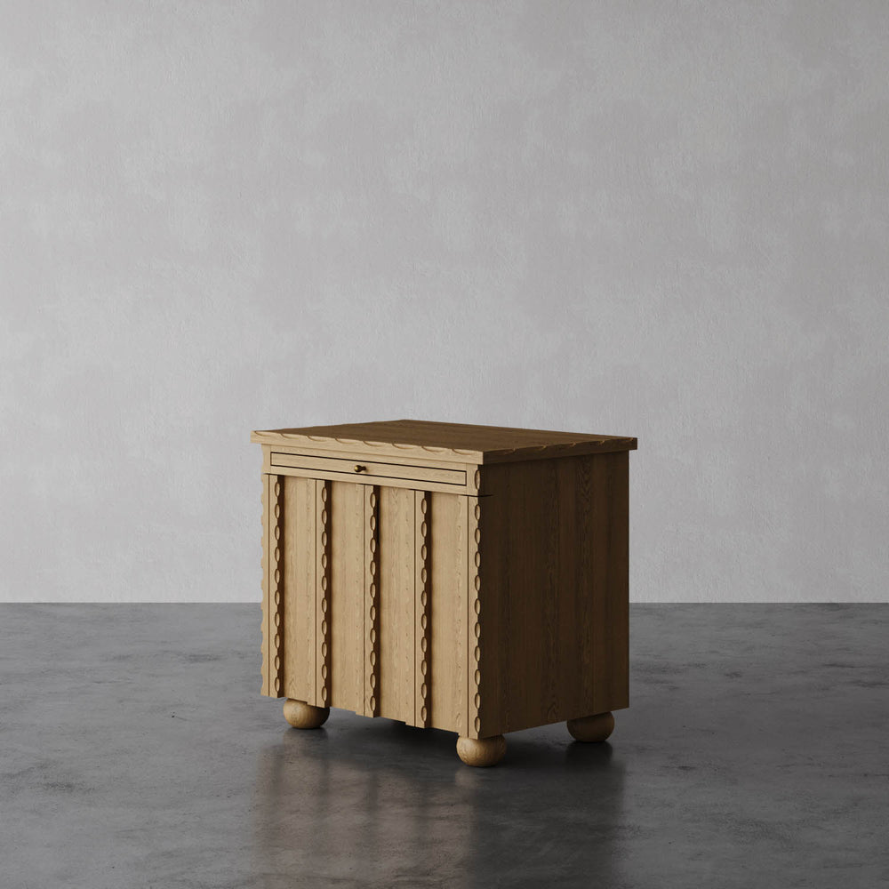 Lemieux et Cie Marchand Nightstand with scalloped edge detailing and textured door fronts, bedside cabinet on rounded feet, shown on polished concrete floor.