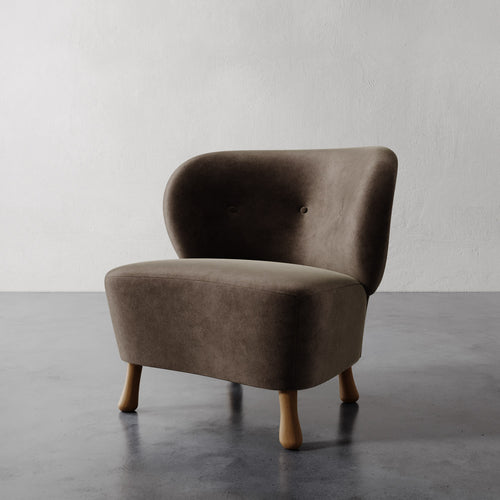 Lemieux et Cie Tourenne Chair with tapered legs in warm taupe upholstery, rounded sculptural form with organic silhouette on concrete flooring against neutral plaster walls.