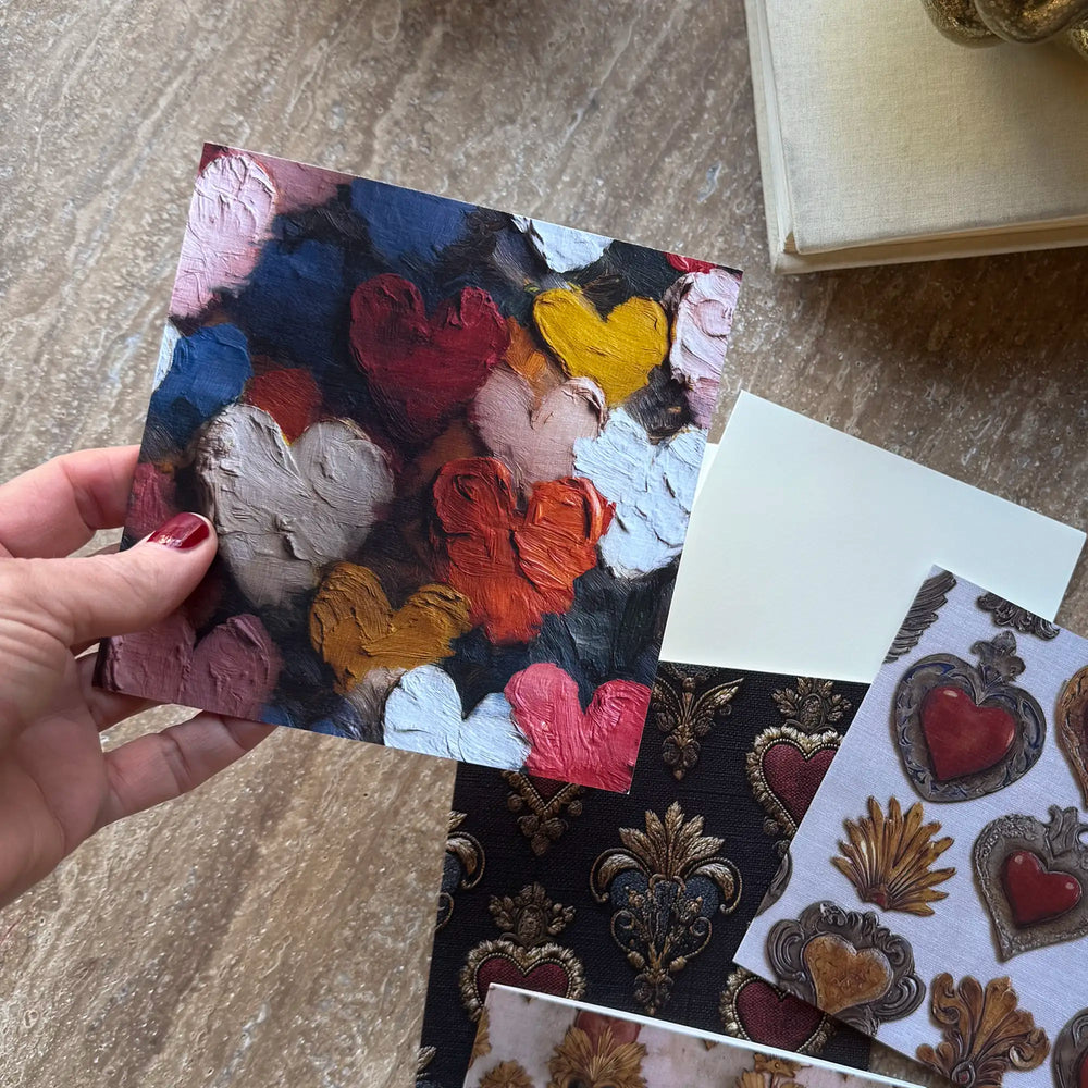 Lemieux et Cie Painterly Hearts Greeting Card Set detail, hand holding colorful heart motif card beside decorative swatches on textured stone surface.