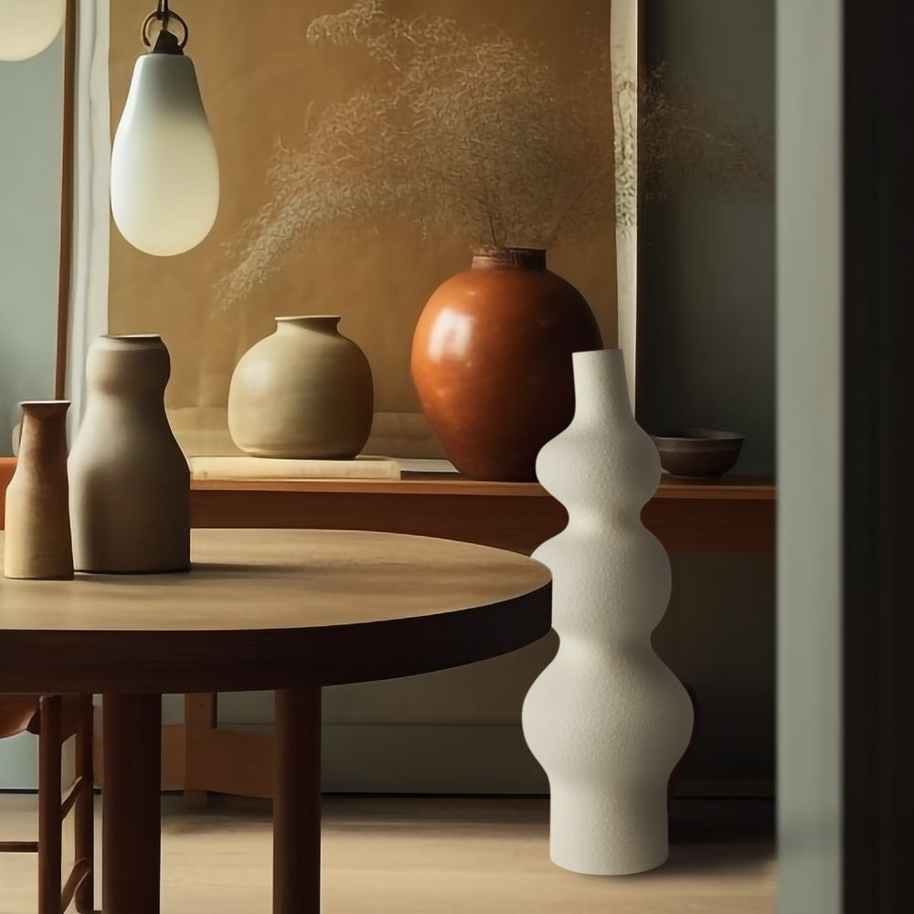 Lemieux et Cie Pasteur Vase in matte white, organic sculptural form with stacked spheres, displayed on round table in warm-toned room with ceramic vases.