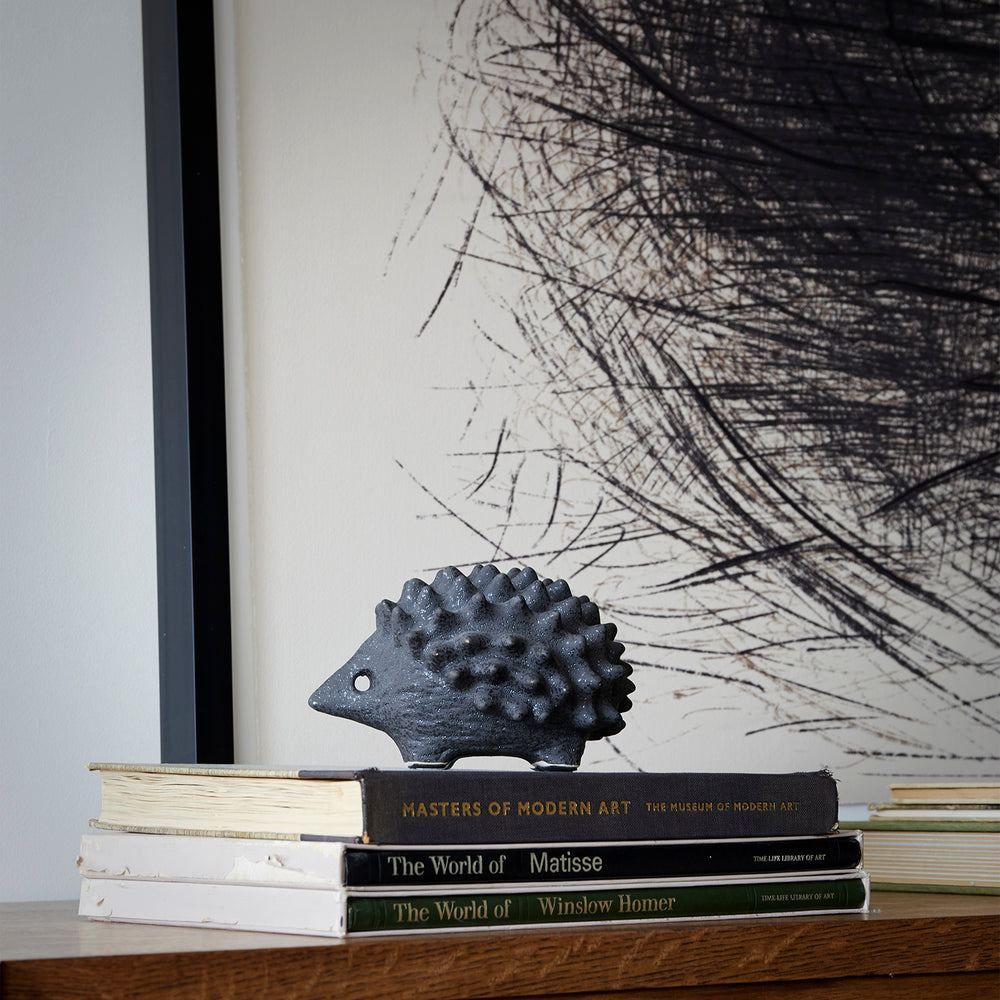 Lemieux et Cie Porcupine in textured black glaze, hand-modeled ceramic sculpture, styled on stacked art books beneath graphic framed artwork on wood surface.