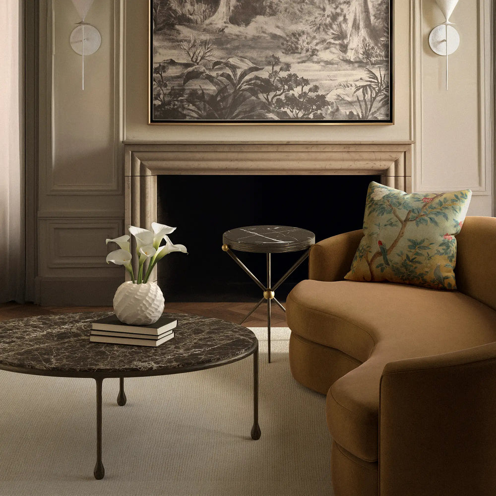 Lemieux et Cie Cambert Round Side Table in bronze iron with aged brass accents and honed Nero Marquina marble top, styled beside fireplace in neutral paneled room.