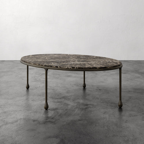Lemieux et Cie Ravelle Oval Coffee Table with Emperador marble top and aged bronze iron frame, shown on polished concrete floor against white walls.