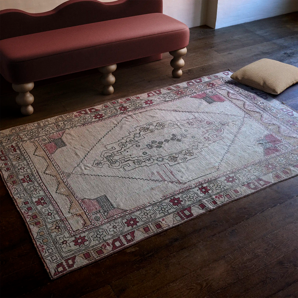 Lemieux et Cie Vintage Anatolian Rug in faded rose and neutral tones, handwoven vintage carpet on dark wood floors beside upholstered bench with turned legs.