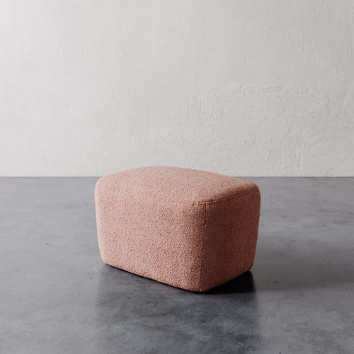 Lemieux et Cie Aurélie Ottoman in blush, rounded rectangular ottoman with soft sculptural form, shown on polished concrete floor against textured plaster wall.