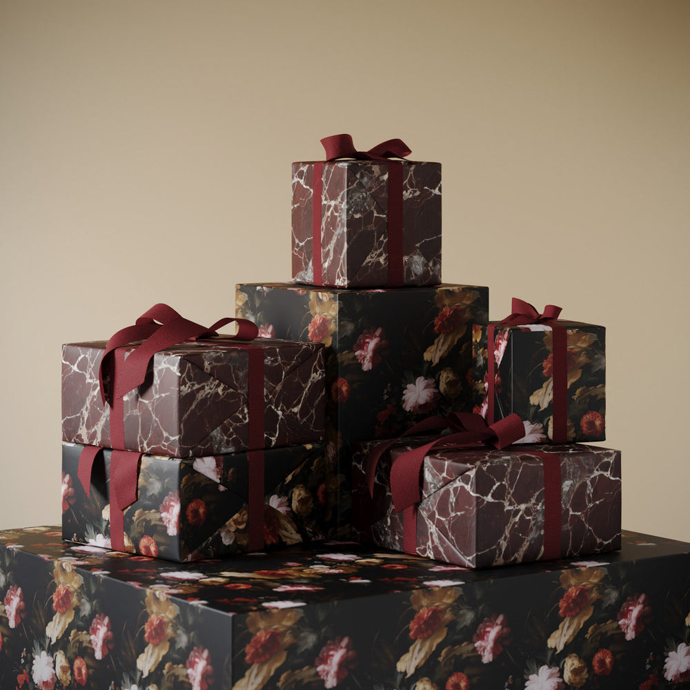 Stack of gifts wrapped in Lemieux et Cie fancy gift wrapping: Floral holiday paper with painterly flowers paired with Rosso Levanto red marble paper.