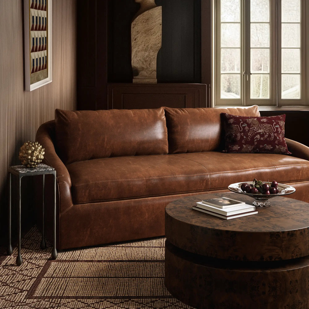 Lemieux et Cie Rousseau Leather Sofa in warm cognac leather, seated beside round coffee table in wood-paneled sitting room with tall windows and woven rug.