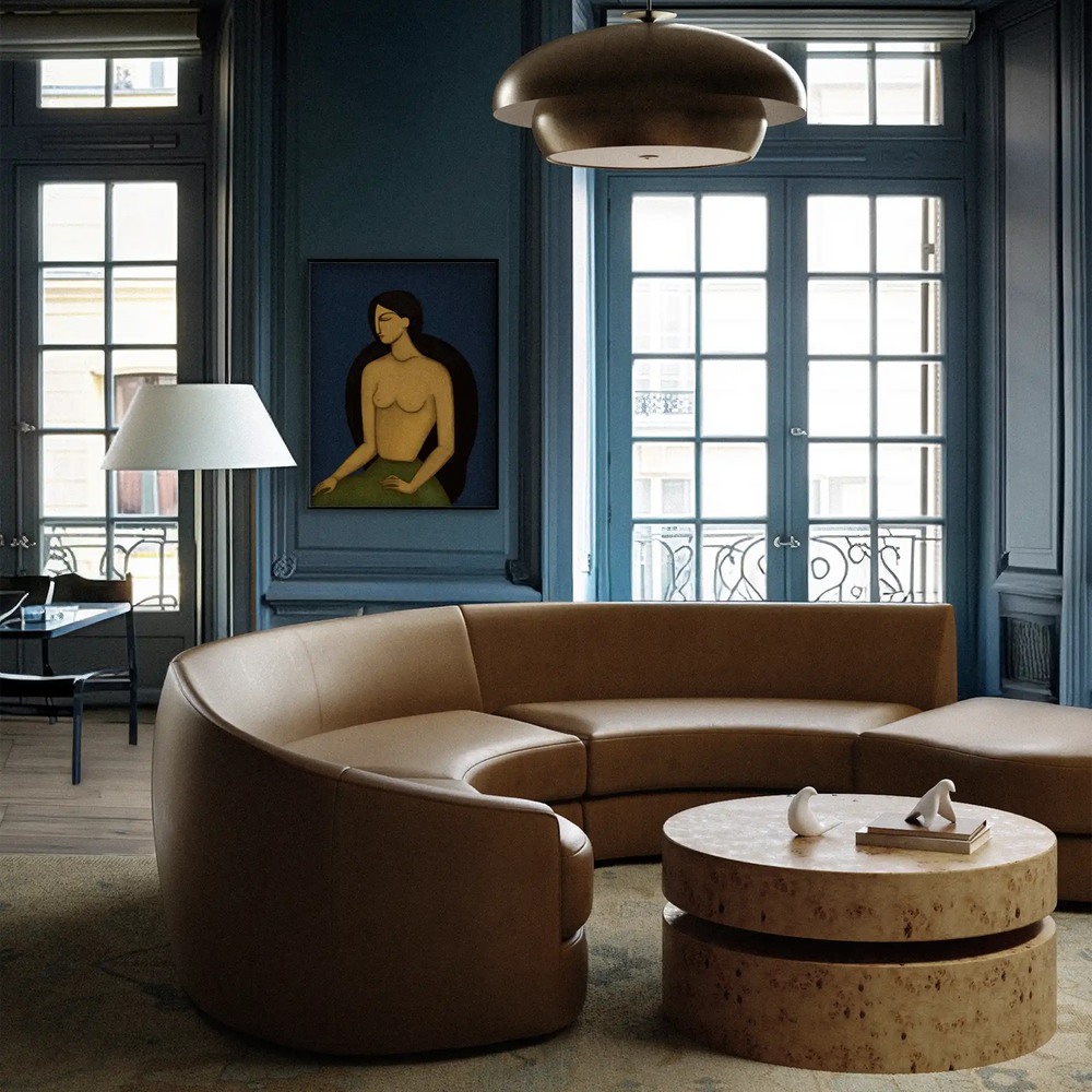 Lemieux et Cie Rulmann Left Ottoman in tan leather, curved sectional seating piece in a room with deep blue painted walls and tall French windows.