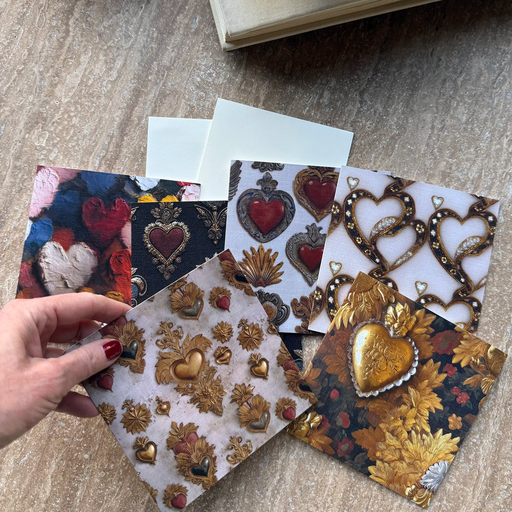 Lemieux et Cie Victorian Locket Greeting Card Set swatches with heart and floral motifs, held in hand on stone floor beside white envelopes.