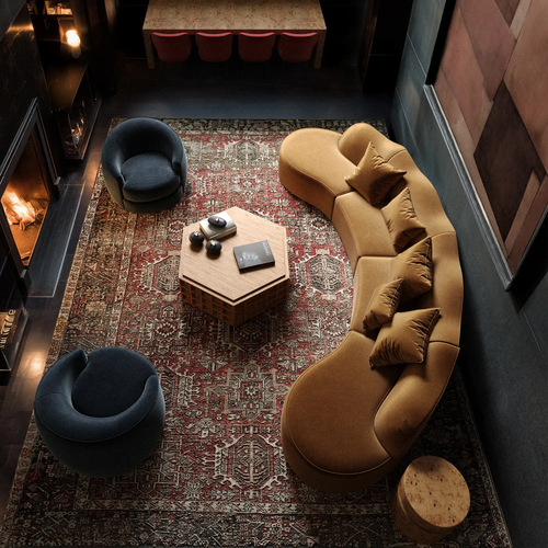 serpentine vintage rug rulmann chair-dubois avenir lehavre rozette chiar Cozy living room with a curved sofa, two blue chairs, and a hexagonal coffee table on a patterned rug.