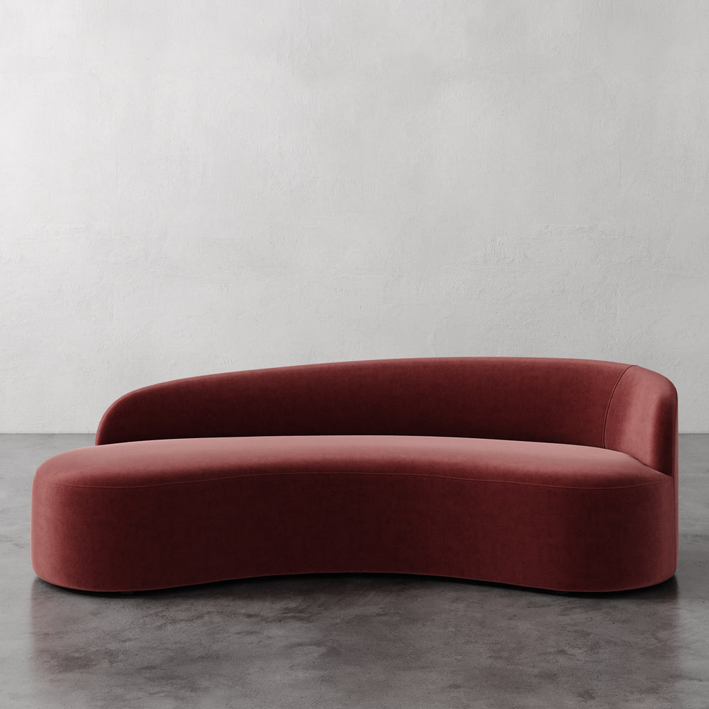 Lemieux et Cie Colette Right Arm Sofa in terracotta upholstery, curved asymmetric sofa with organic sculptural form, on concrete floor against white walls.