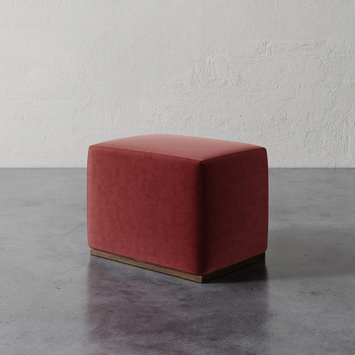Lemieux et Cie Sophie Rectangular Ottoman in terracotta upholstery with plinth base, compact seating on concrete floor against textured plaster walls.