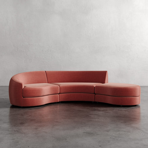 Curved pink sofa on a gray floor with a plain white wall background Rulmann 3-Piece Left Sectional Sienna