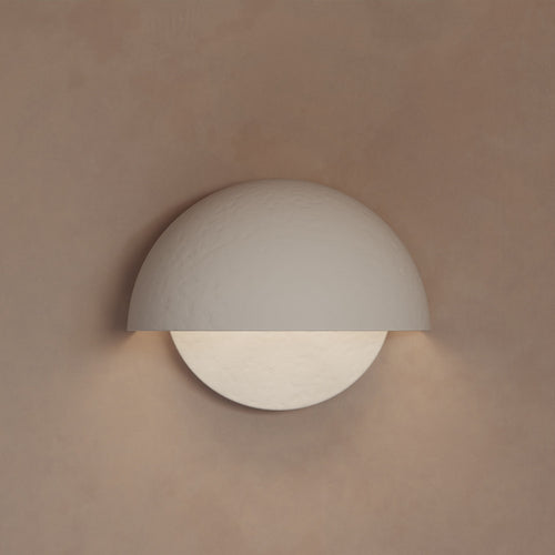 Lemieux et Cie Argan sconce in plaster, circular wall-mounted fixture with warm light, shown on neutral blush-toned wall.