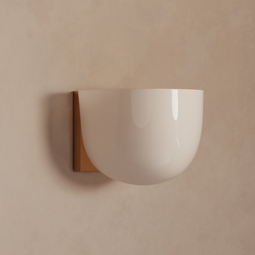 Lemieux et Cie Cheverny Sconce with rounded white glass shade and warm brass backplate, wall-mounted on neutral plaster wall in soft light.