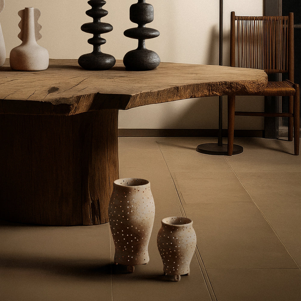 Lemieux et Cie Yassine Candle Holder in beige ceramic with pierced dot pattern, decorative vessel on stone floor beside live-edge wood table and chair.