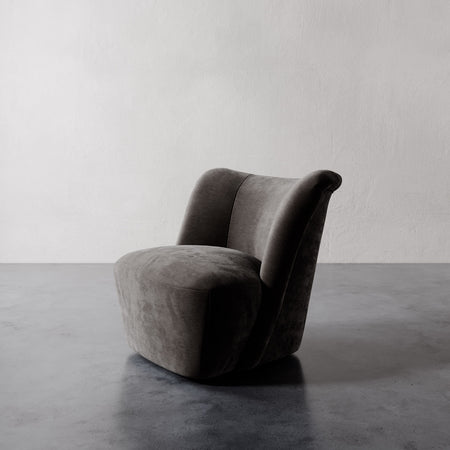 Lemieux et Cie Aurélie Swivel Chair, sculptural rounded form with rolled back in charcoal upholstery, shown on polished concrete floor against textured plaster wall.