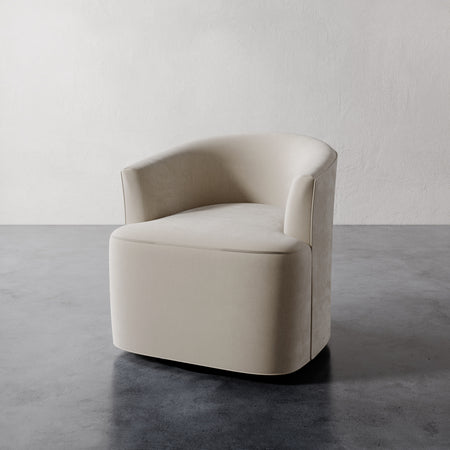 Lemieux et Cie Garnier Swivel Chair in warm neutral upholstery, rounded sculptural silhouette on stone flooring against white plaster walls.