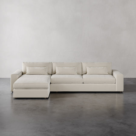 Lemieux et Cie Lacroix Left Chaise Sectional in ivory, low-profile modular sofa with bolster pillows on gray concrete floor against neutral walls.