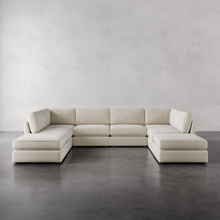 Lemieux et Cie Chanaux 8-Pc Sectional in cream, modular sofa with dual chaises, shown on polished concrete floor against white plaster walls.