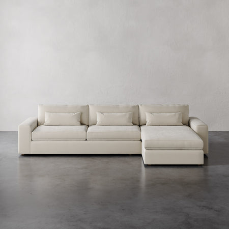 Lemieux et Cie Lacroix Right Chaise Sectional in ivory, low-profile modular sofa with bolster pillows, shown on polished concrete floor against textured plaster walls.