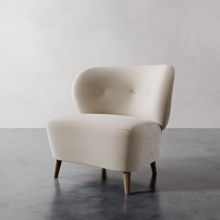 Lemieux et Cie Tourenne Chair with tapered legs in ivory upholstery, rounded sculptural slipper chair with button tufting, shown on concrete floor against textured plaster walls.