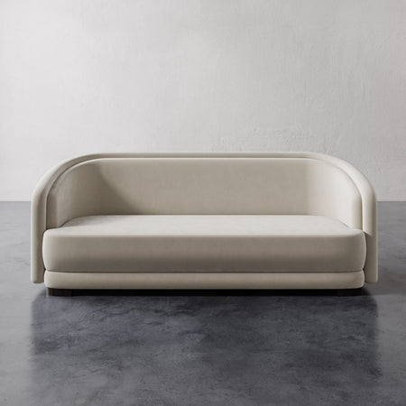 Lemieux et Cie Valence Sofa in warm neutral upholstery, sculptural rounded form with low profile, shown on polished concrete floor against white walls.
