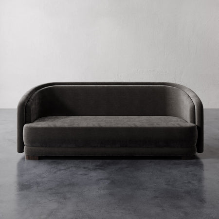 Lemieux et Cie Valence Sofa in charcoal, low-profile rounded sofa on dark stone floor against white plaster wall.