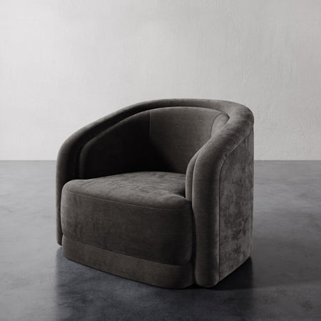 Lemieux et Cie Valence Swivel Chair in charcoal, low-profile barrel chair with sculptural rounded arms, shown on concrete floor against white walls.