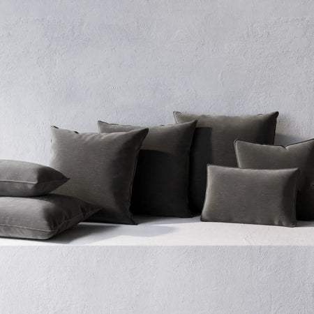 Lemieux et Cie Throw Pillows in charcoal and olive tones, welted cushions in various sizes, arranged on white textured plaster surface.