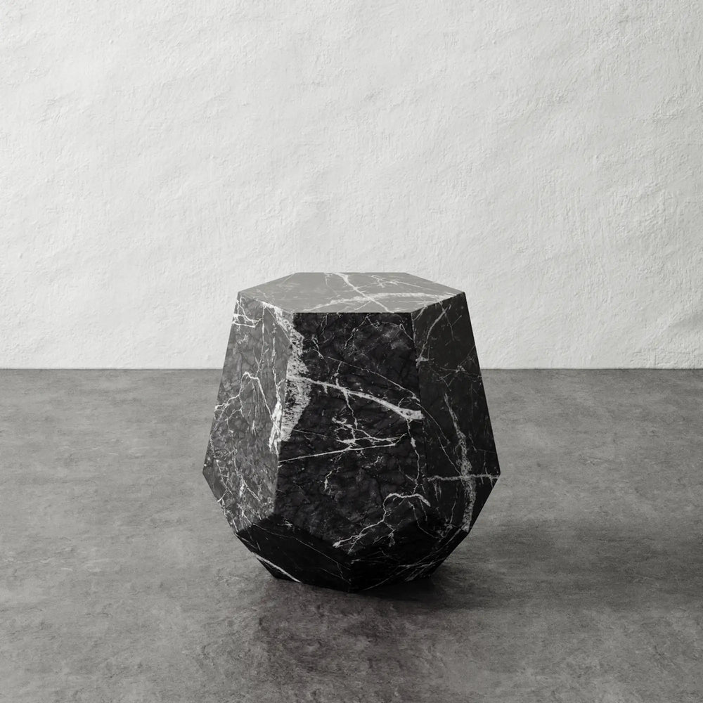 Lemieux et Cie Tessaire Faux Marble Accent Table in dark veining, sculptural faceted form on concrete floor against textured white plaster walls.