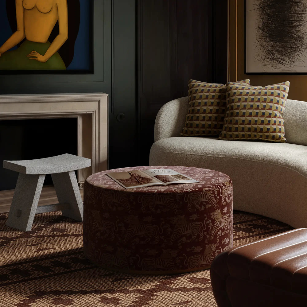 Lemieux et Cie Pierre Hair-on-Hide Stool in patterned burgundy and cream, upholstered ottoman styled in sitting room with dark paneled walls and wood floors.