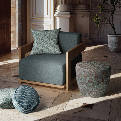 Taiko Stool / End Table by Lemieux et Cie in Oxidized Jade reactive glaze with rounded form and aged-metal green and oxblood tones next to a teak outdoor chair surrounded by patterned pillows