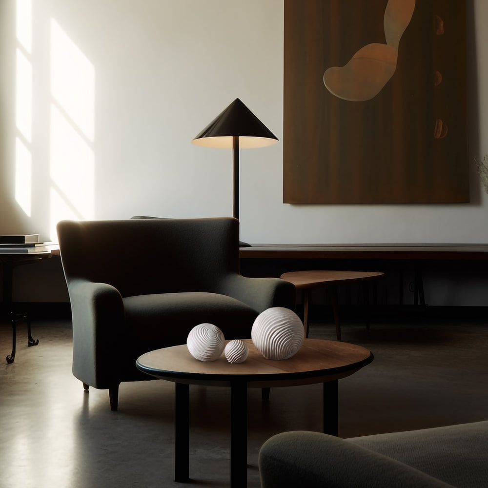 Lemieux et Cie Varenne Sphere in matte ceramic with etched surface, sculptural sphere displayed on round wood table in a shadowed sitting room with dark upholstered seating and warm daylight.